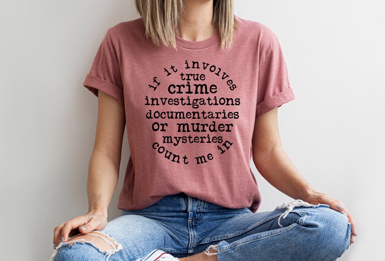 May include: A pink t-shirt with the text "If it involves true crime investigations documentaries or murder mysteries count me in" printed on it.
