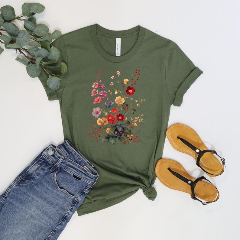 May include: A green short-sleeved t-shirt with a floral print featuring a variety of colors, including red, pink, yellow, blue, and green. The shirt is made of a soft, comfortable fabric and has a relaxed fit.