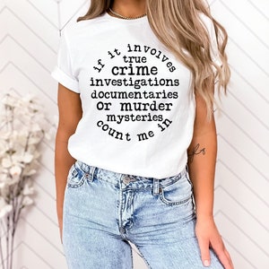 May include: White t-shirt with black text that reads "If it involves true crime investigations, documentaries, or murder mysteries, count me in."