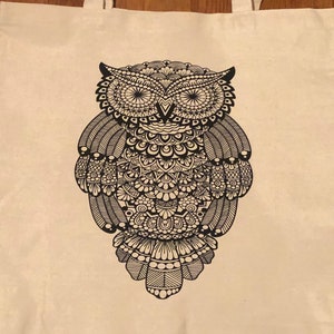 May include: A white canvas tote bag with black straps and a black and white mandala-style owl design.