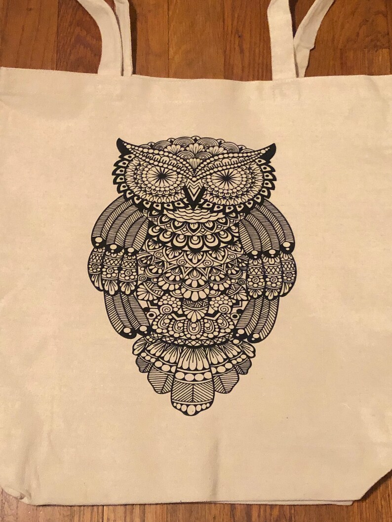 May include: A white canvas tote bag with black straps and a black and white mandala-style owl design.