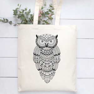 May include: A white tote bag featuring a black and white owl design. The owl is intricately patterned and has large, round eyes.