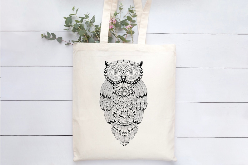 May include: A white tote bag featuring a black and white owl design. The owl is intricately patterned and has large, round eyes.