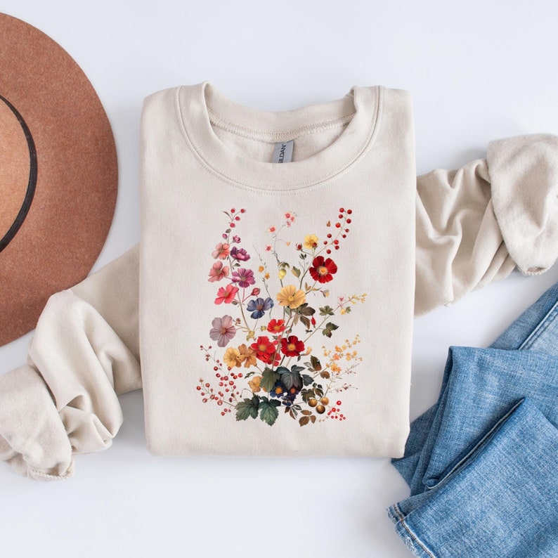 May include: A beige sweatshirt with a floral print featuring a variety of colorful flowers, including red, yellow, orange, purple, and pink.