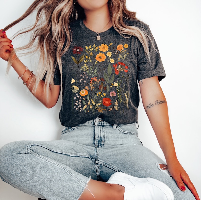 May include: A gray t-shirt with a floral print featuring various colors, including red, orange, yellow, and green. The shirt has a crew neck and short sleeves.