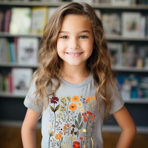 May include: A young person wearing a grey t-shirt with a floral print featuring various colors, including red, orange, yellow, and green.