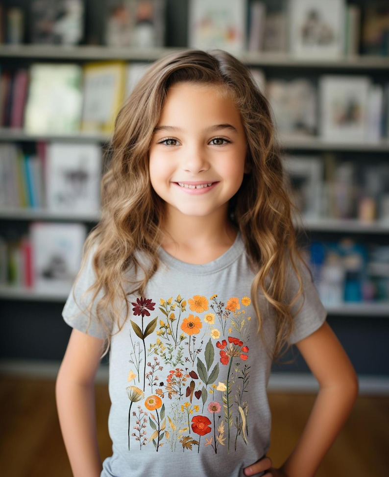 May include: A young person wearing a grey t-shirt with a floral print featuring various colors, including red, orange, yellow, and green.