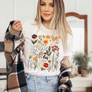 May include: A white t-shirt with a colorful floral print featuring various flowers, leaves, and stems in shades of red, orange, yellow, and green.