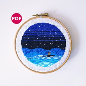 May include: A cross-stitch pattern of a person swimming in the ocean at night under a starry sky. The pattern is framed in a wooden hoop.