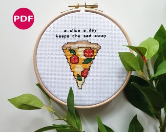 May include: A white embroidery hoop with a cross-stitch design of a pizza slice with the text "a slice a day keeps the sad away".