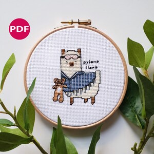May include: A cross-stitch pattern of a llama wearing a blue and white pajama with a teddy bear in its arms. The text "rujana llama" is stitched above the llama.