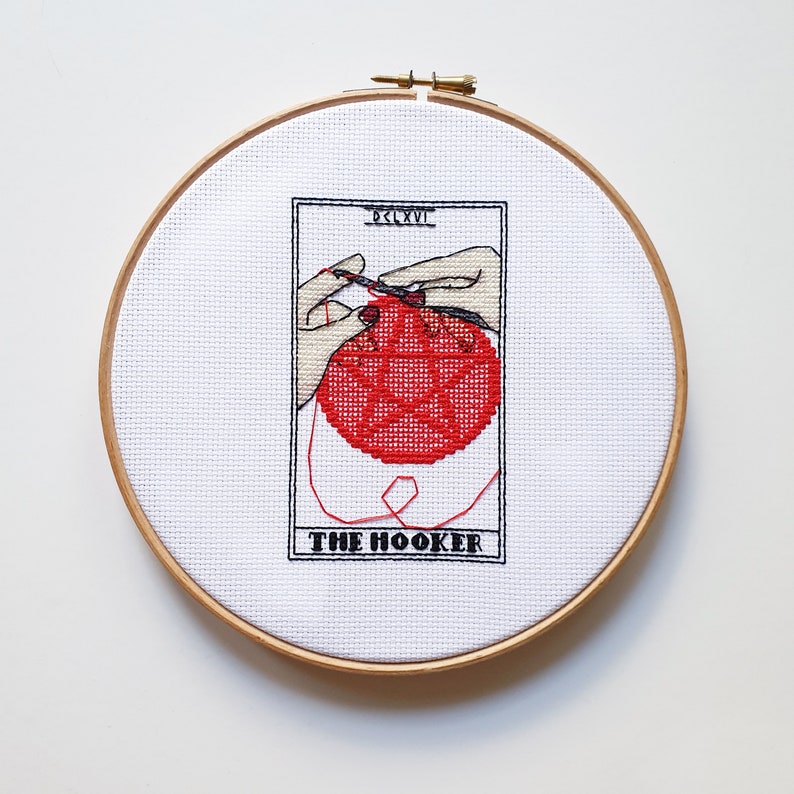Cheeky feminist cross stitch wall art shown framed, with the words 'The Hooker' in a tarot card style design. The same image as before is shown, just without the tarot cards behind the embroidery hoop.
