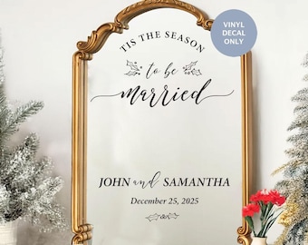 May include: A gold-framed mirror with a vinyl decal that reads "Tis the season to be married" with holly sprigs and berries. Below the text is "John and Samantha" and "December 25, 2025".