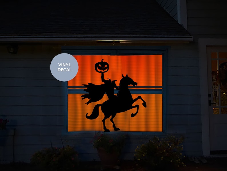 Puede incluir: Un vinilo adhesivo negro aplicado en una ventana, con la silueta de un jinete sin cabeza montando un caballo encabritado y sosteniendo una calabaza tallada. La ventana brilla con una luz naranja y el texto VINYL DECAL es visible.