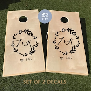 May include: Two wooden cornhole boards with a black vinyl decal of a wreath with the letters Z and K and the text "est. 2025". The decal is a set of two.