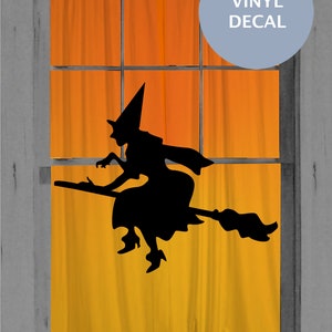 Puede incluir: Un adhesivo de vinilo negro con la silueta de una bruja volando sobre una escoba, colocado sobre una ventana con cortinas naranjas. Una insignia circular azul claro en la esquina superior derecha contiene el texto blanco VINYL DECAL en mayúsculas.