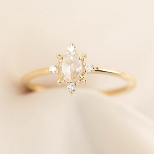 May include: A gold ring with a round, clear gemstone surrounded by smaller diamonds. The ring is set on a white background.