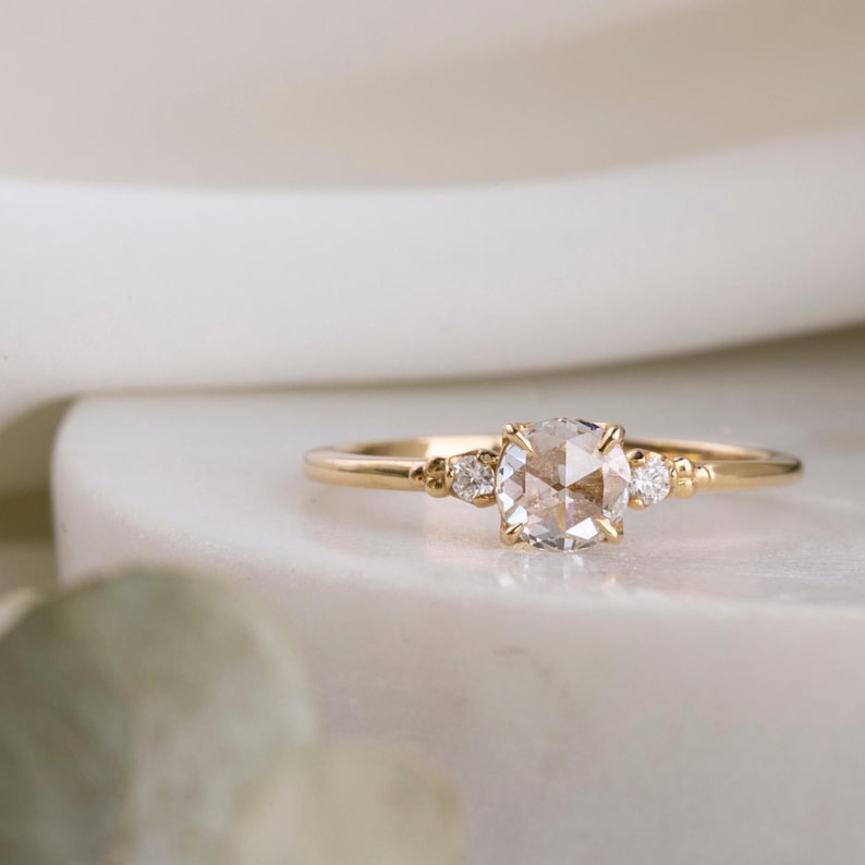 May include: A delicate gold ring with a round, clear, rose-cut diamond center stone and two smaller accent diamonds on either side.