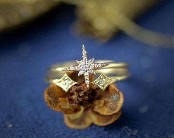 May include: A gold ring with a diamond star design. The ring is stacked on top of two other gold rings. The rings are on a blue surface.
