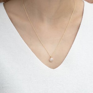 May include: A delicate gold chain necklace with a small round pendant featuring a clear crystal surrounded by a halo of smaller crystals.