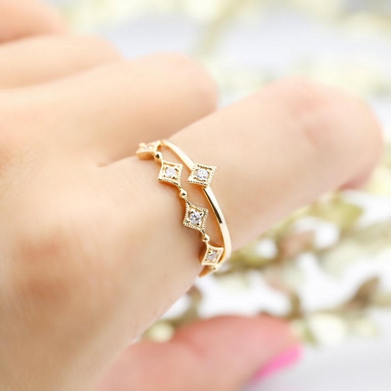 May include: A gold ring with a delicate design featuring small diamonds set in square shapes. The ring is worn on a finger.