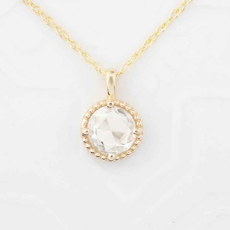 May include: A gold chain necklace with a pendant featuring a clear round gemstone set in a beaded bezel.