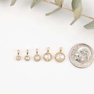 May include: Five gold pendants with different sized clear round gemstones. The pendants are arranged in a row from smallest to largest. A US dime is included for size comparison.