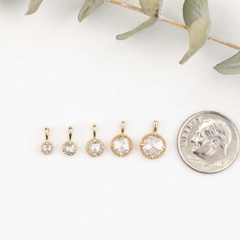 May include: Five gold pendants with different sized clear round gemstones. The pendants are arranged in a row from smallest to largest. A US dime is included for size comparison.
