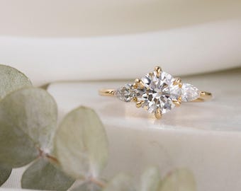 May include: A gold engagement ring with a large round center diamond and two pear-shaped side diamonds.