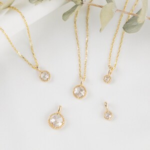 May include: Four gold necklaces with different sized round clear gemstone pendants. The pendants have a textured gold border.