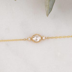 May include: A delicate gold chain bracelet with a single oval-shaped diamond set in a bezel setting. Two smaller diamonds flank the center stone.