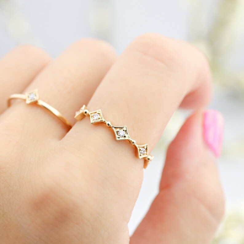May include: A gold ring with a delicate design featuring a row of small diamonds set in square shapes.