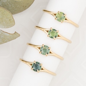 May include: Four gold rings with green gemstones. Each ring has a split band design with a round gemstone in the center.