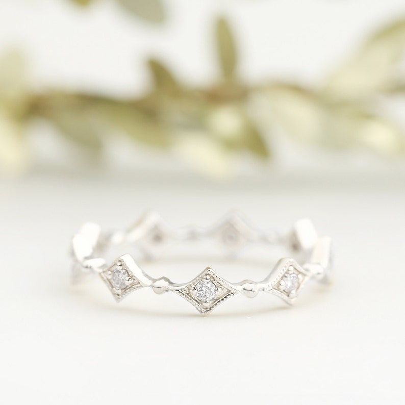 May include: A delicate silver band ring with a row of small, square-shaped diamonds set in a scalloped design.
