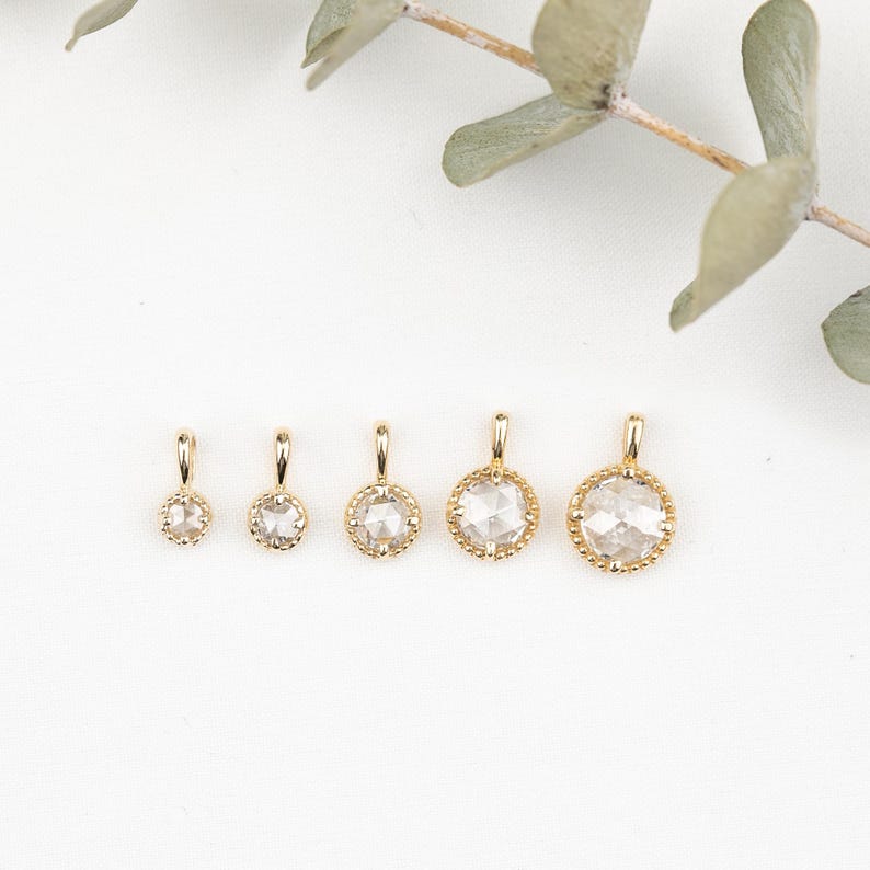 May include: Five gold pendants with different sized clear round rose cut diamonds. The diamonds are set in a gold bezel setting with a decorative edge.
