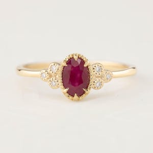 May include: A gold ring with a red ruby gemstone and small diamonds set in a delicate floral design.