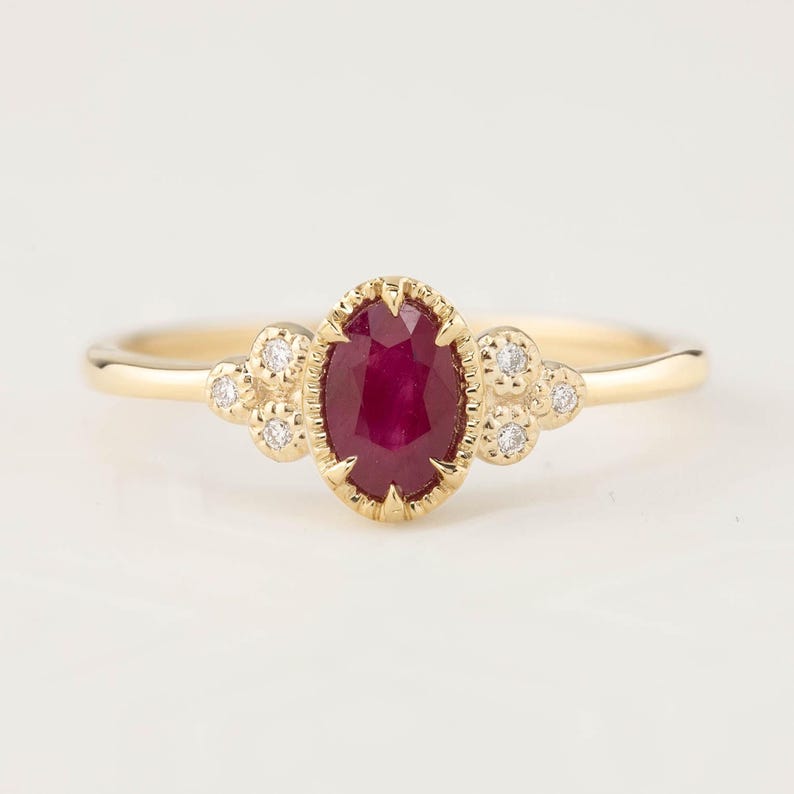 May include: A gold ring with a red ruby gemstone and small diamonds set in a delicate floral design.