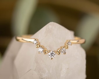 May include: A delicate gold band with a curved row of small diamonds, set on a white crystal surface.
