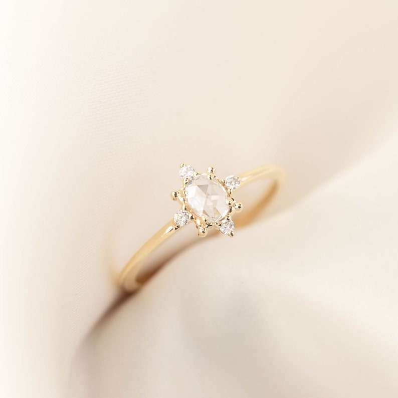 May include: A gold ring with a large, oval-shaped, clear gemstone surrounded by smaller, clear gemstones.