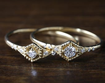 May include: Two gold rings with a diamond in each. The diamonds are set in a geometric design with smaller diamonds surrounding them.