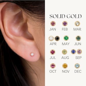 May include: A close-up of a person's ear with a small diamond stud earring. The image also shows a chart of birthstone colors for each month of the year, labeled "SOLID GOLD".
