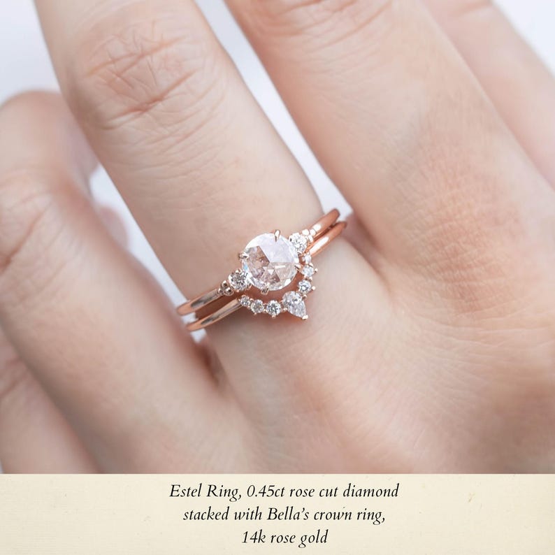 May include: A rose gold engagement ring with a 0.45 carat rose cut diamond center stone. The ring is stacked with a smaller rose gold band featuring a crown of smaller diamonds. The text "Estel Ring, 0.45ct rose cut diamond stacked with Bella's crown ring, 14k rose gold" is visible below the ring.
