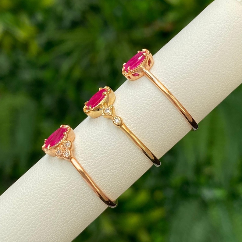 May include: Three gold rings with red gemstones and small diamonds. The rings are displayed on a white surface.