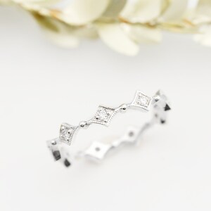 May include: A delicate silver band ring with a row of small, square-shaped diamonds set in a scalloped design.
