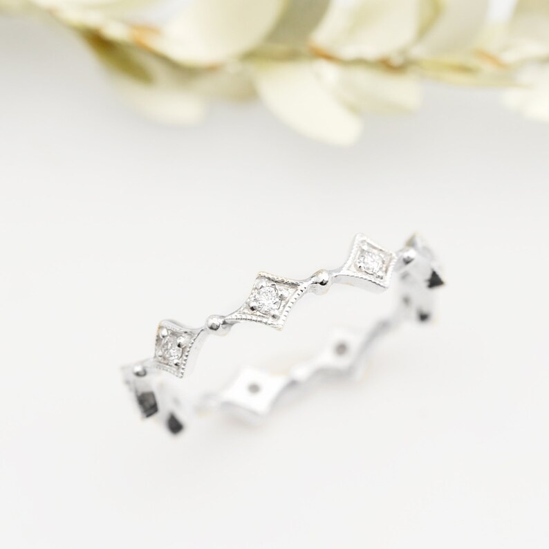 May include: A delicate silver band ring with a row of small, square-shaped diamonds set in a scalloped design.