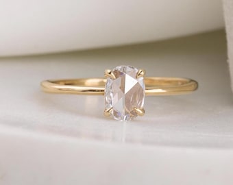 May include: A gold band ring featuring a clear oval-shaped gemstone. The gemstone has a faceted cut and is set in a simple prong setting.