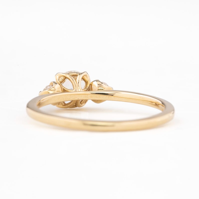 May include: A delicate gold ring with a floral design and three small diamonds. The ring is shown from the side, highlighting the intricate details of the band.