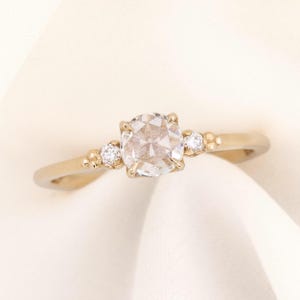 May include: A gold engagement ring with a round, clear center stone and two smaller accent stones on the band.