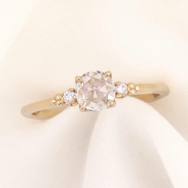 May include: A gold engagement ring with a round, clear center stone and two smaller accent stones on the band.