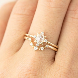 May include: A delicate gold ring set with a round, clear, rose-cut diamond surrounded by smaller diamonds. The ring is worn on a finger.